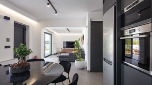 A modern kitchen with a built-in oven, a dining area with a table and chairs, and a living room with a sofa and a flat-screen TV. - Horizon Villa Oasis, Walk to Platanias Beach! (Chania)