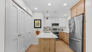 Una cocina moderna con armarios blancos, una isla de madera, electrodomésticos de acero inoxidable y una lámpara colgante.
