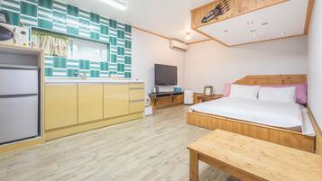 Habitación de hotel compacta con kitchenette, una cama con cabecera de madera, una mesita de madera y un televisor.
