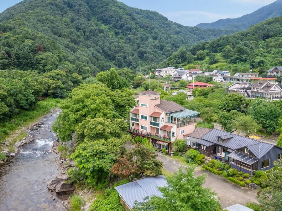 A residential area with houses, a river, and a forested mountain backdrop.
