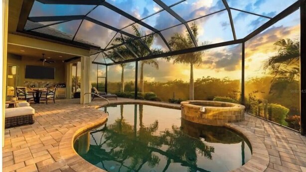 A modern indoor swimming pool with a glass ceiling, surrounded by a patio area with seating and a view of palm trees. - Eight Palms/ Punta Gorda Waterfront Paradise Escape (Punta Gorda)