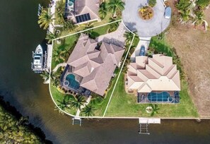 Vista aérea de una propiedad residencial que incluye una casa grande, una piscina y un muelle con un barco.