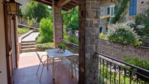 Une terrasse couverte avec un mur en pierre, une table blanche et une rambarde en métal.