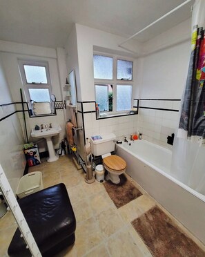 A bathroom with a toilet, sink, and bathtub. There are windows, a mirror, and a shower curtain.