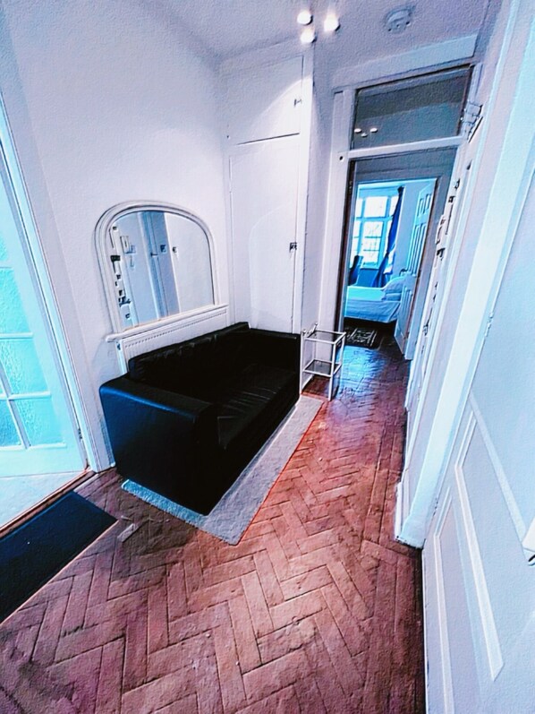 A hallway with a black sofa, a white door, and a herringbone-patterned floor.