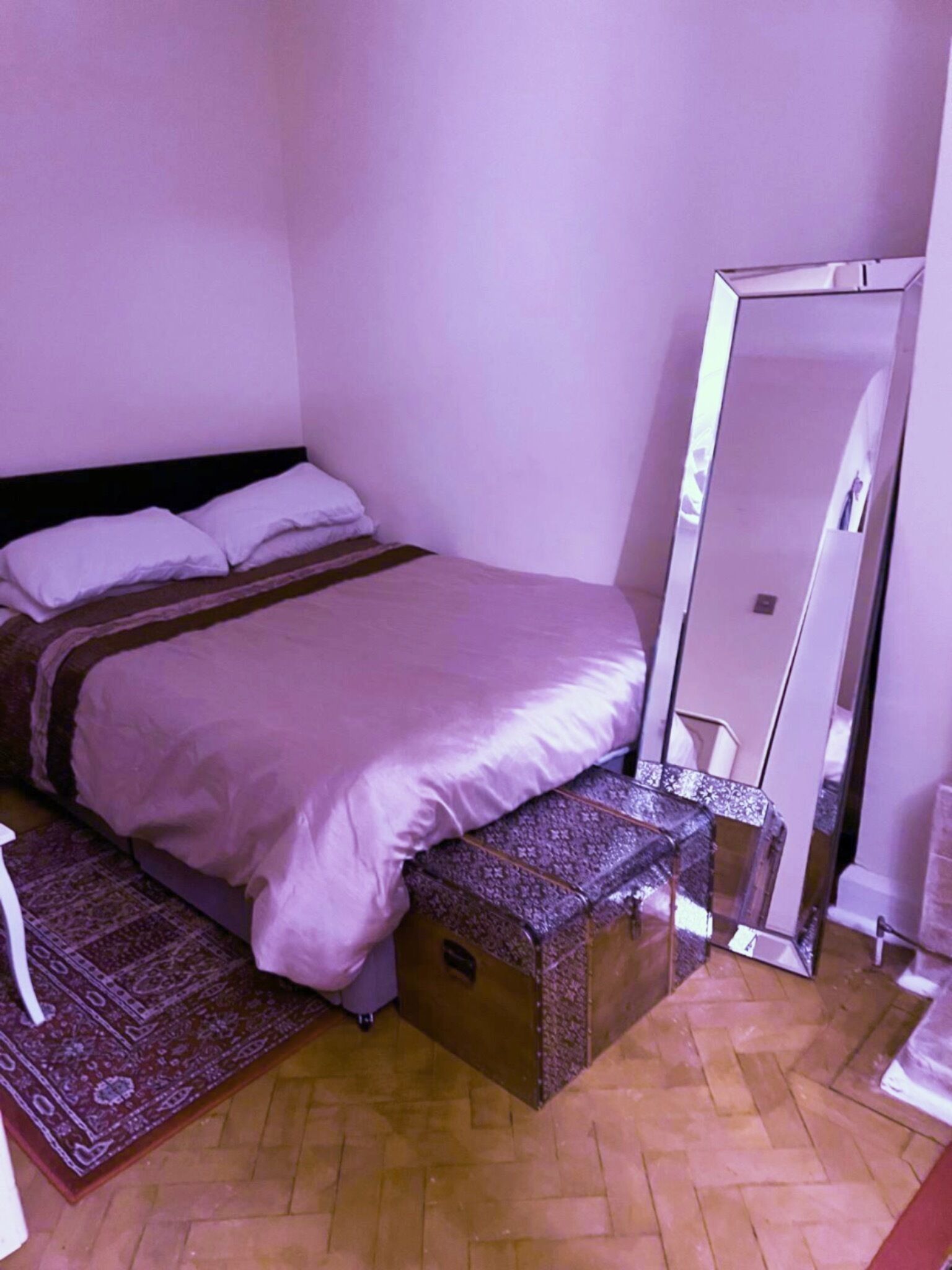 A bedroom with a bed, a mirror, and a patterned rug.