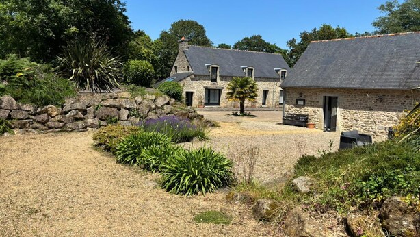 A stone building with a sloped roof, surrounded by a gravel courtyard and various plants. - LE JARDIN SAINT-GERMAIN Lodges & Events (Plogastel-Saint-Germain)