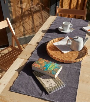 Une table en bois sur laquelle se trouve un set de table en fibres tressées, un livre intitulé « FAROE ZUR LAGE », une théière et une tasse posée sur une soucoupe.