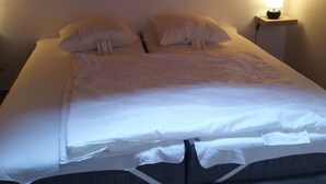 Ein ordentlich bezogenes Bett mit weißen Leinen und Kissen, ein Nachttisch mit Lampe und eine Holzbalkendecke.
