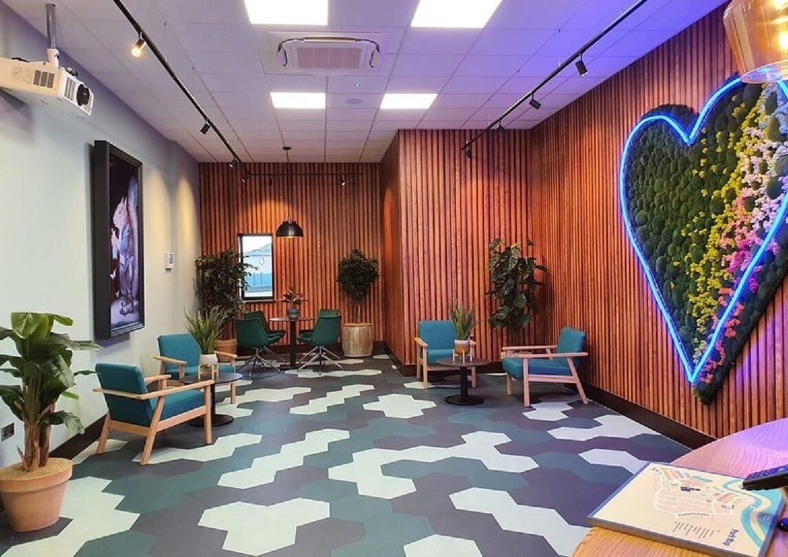 A modern waiting area with a heart-shaped floral wall, comfortable seating, and a projector screen.