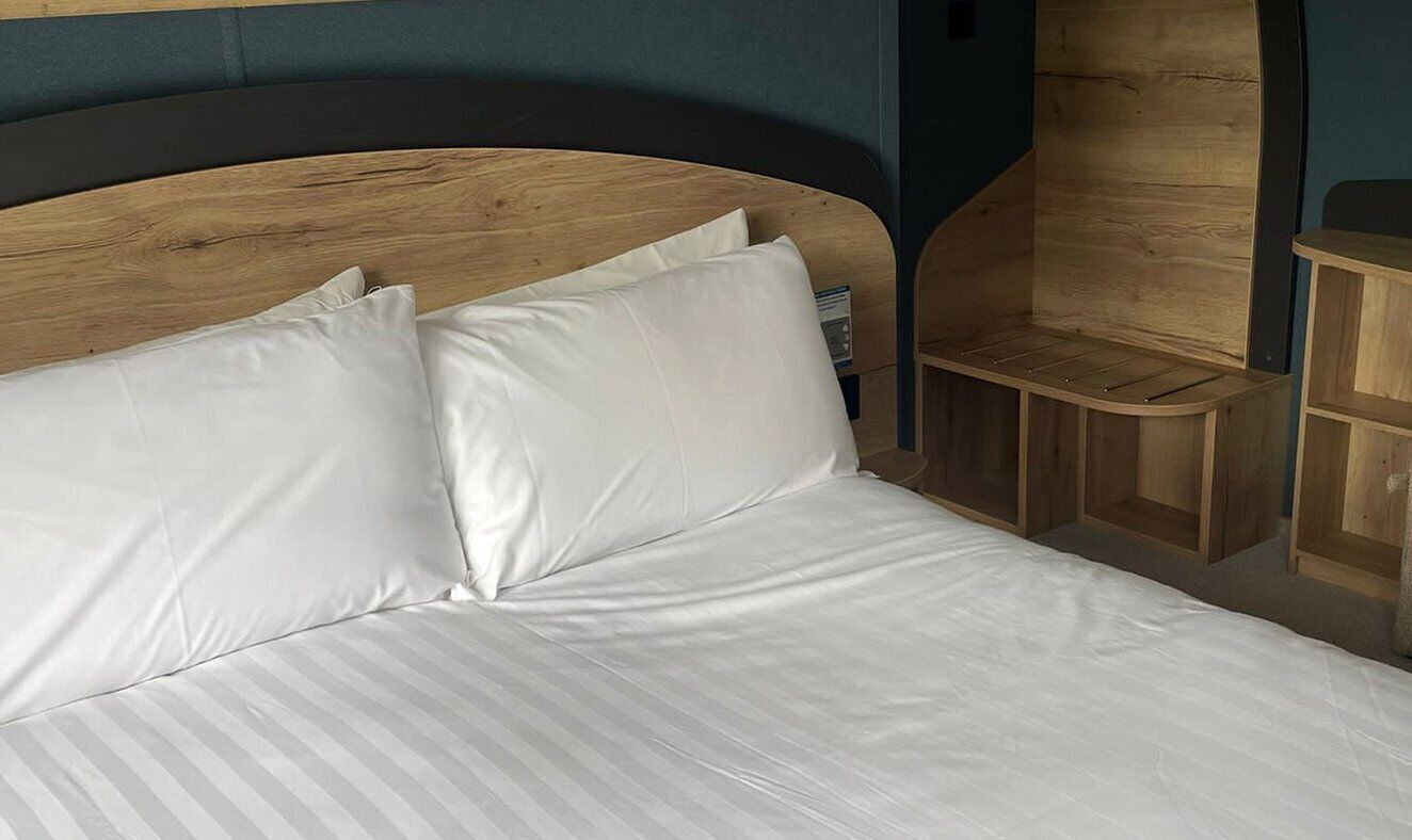 A bed with white linens and a wooden headboard.
