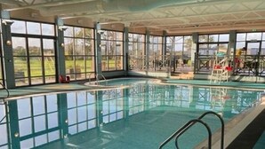 Ein Hallenbad mit großen Glaswänden, einem Sprungbrett und einem Rettungsschwimmerstuhl.