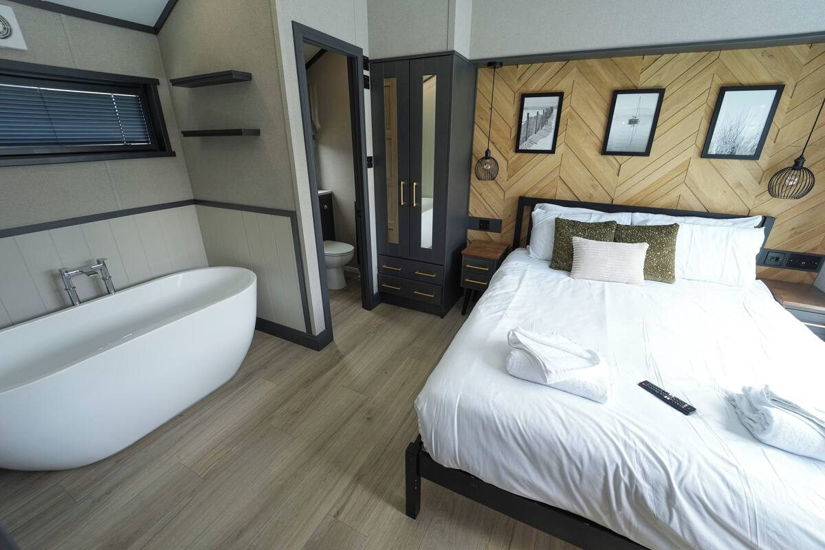 A modern bedroom with a large bed, a built-in bathtub, and a wooden herringbone wall pattern.