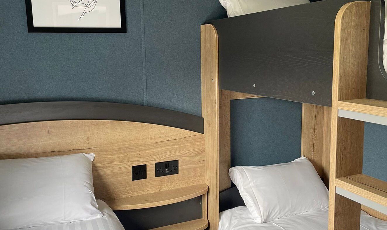 Una cama individual con dos literas, cabecera de madera y un almohadón blanco.