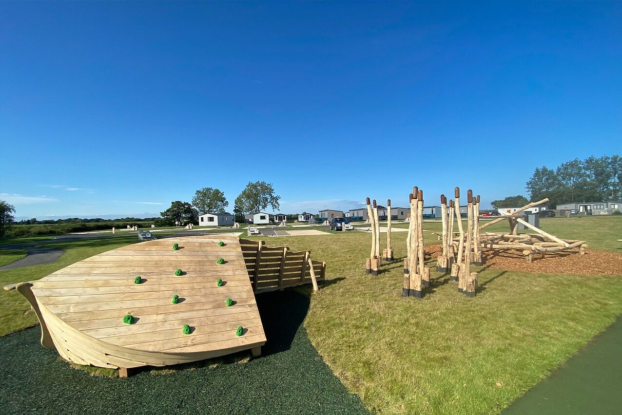 Una estructura de juego de madera con puntos de agarre para escalar y un tobogán.