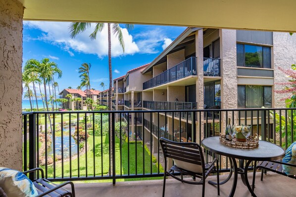 A balcony with a view of a pool, palm trees, and a building with multiple balconies.