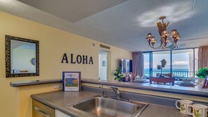 A modern kitchen with a stainless steel sink, a framed picture on the counter, and a view of the ocean through large windows. - Direct oceanfront resort offers great ocean views (Lahaina)