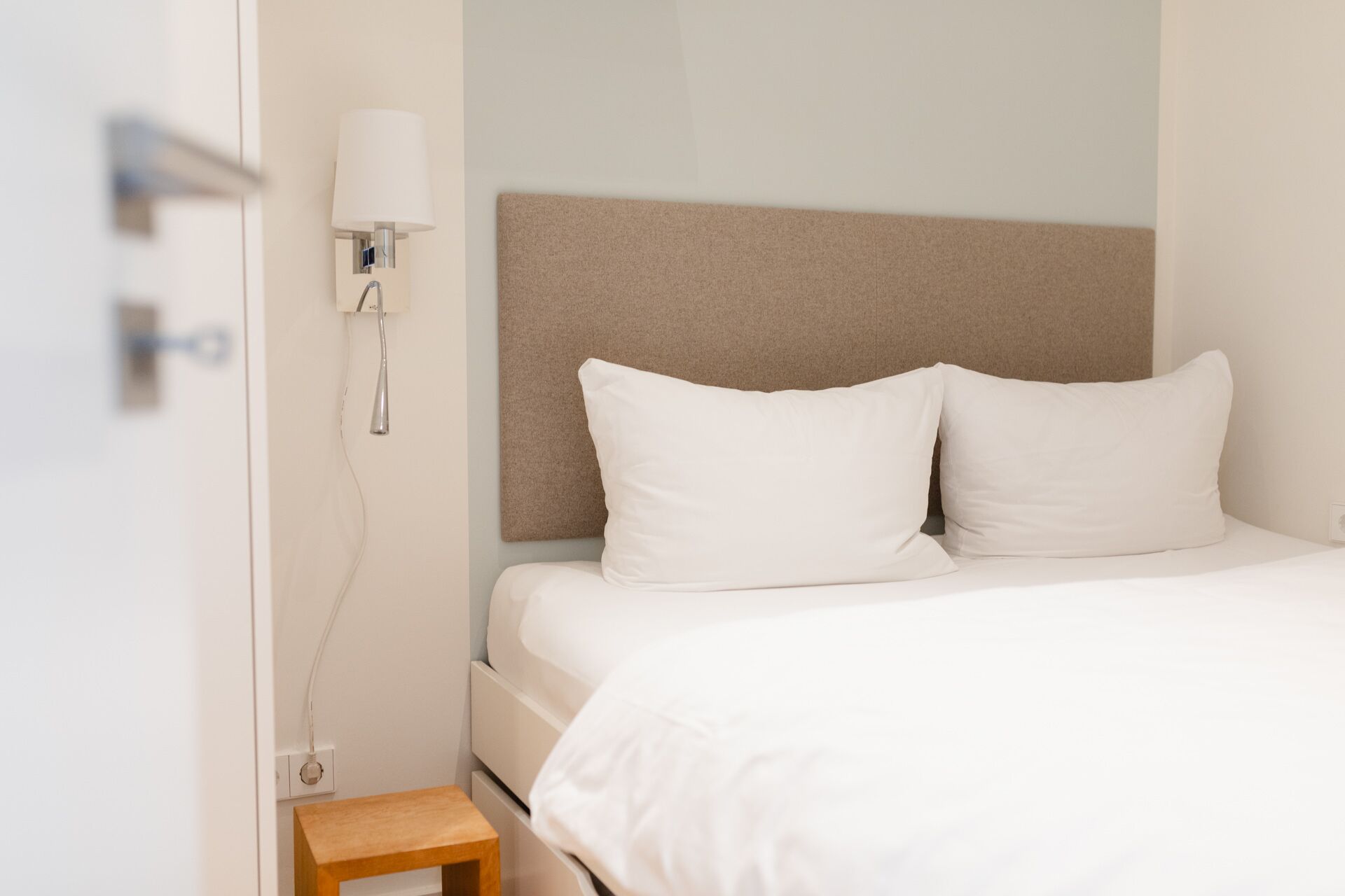 A hotel room with a bed, a nightstand, a lamp, and a wall-mounted light fixture.