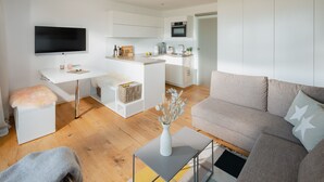 Un salon moderne avec un canapé, une table basse et un téléviseur. Il y a également un coin cuisine équipé de placards et d’un évier.