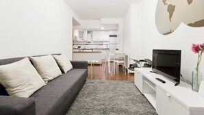 En moderne stue med en grå sofa, et fladskærms-tv og et lille spiseområde i baggrunden.