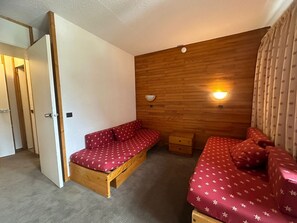A cozy room with a wooden wall, a sofa, a bed, and a small wooden chest. - Divisible studio 4 ppl, ski-in, balcony (Plagne Bellecôte)