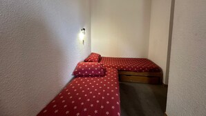 A small, narrow room with two single beds, each with red bedding and star patterns.