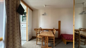 A dining area with a wooden table and chairs, a bench, a television, and a ceiling fan.
