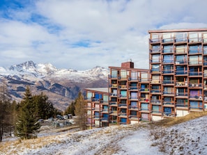 Um edifício de vários andares com varandas, com montanhas nevadas ao fundo.