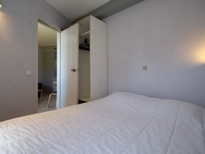 Quarto com uma cama grande, um guarda-roupa e uma porta que dá para outro cômodo.