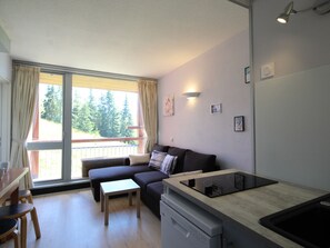 Uma sala de estar moderna com sofá, uma mesa pequena, área de cozinha com pia e varanda com guarda-corpo.