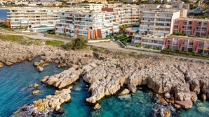 Zona residencial costera con edificios de varios pisos, costa rocosa y aguas azul turquesa.
