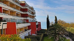 Un hotel de varios pisos con balcones, un jardín cuidado y vistas al mar.