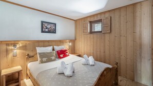 Quarto com cabeceira de madeira, cama com roupa de cama branca, mesa de cabeceira pequena e janela com persianas de madeira.