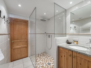 A modern bathroom with a shower, a wooden door, a sink with a granite countertop, and a mirror.