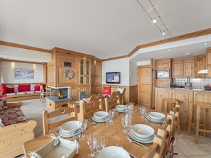 A spacious living area with a wooden dining table set for a meal, wooden cabinets, and a fireplace.