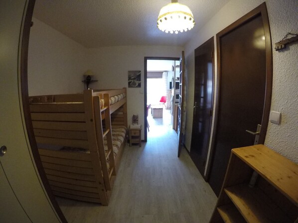 A narrow hallway with bunk beds on the left, a wooden bench on the right, and a door at the end.