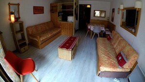 A compact living space with a wooden sofa, a red chair, a small table, and a kitchenette area. - Studio cabin for 4 people, south-facing, balcony (Valloire)