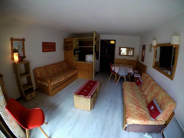 Ein gemütlicher, kompakter Wohnbereich mit Holzsofa, einem roten Sessel, einem kleinen Tisch und einer Küchenzeile.