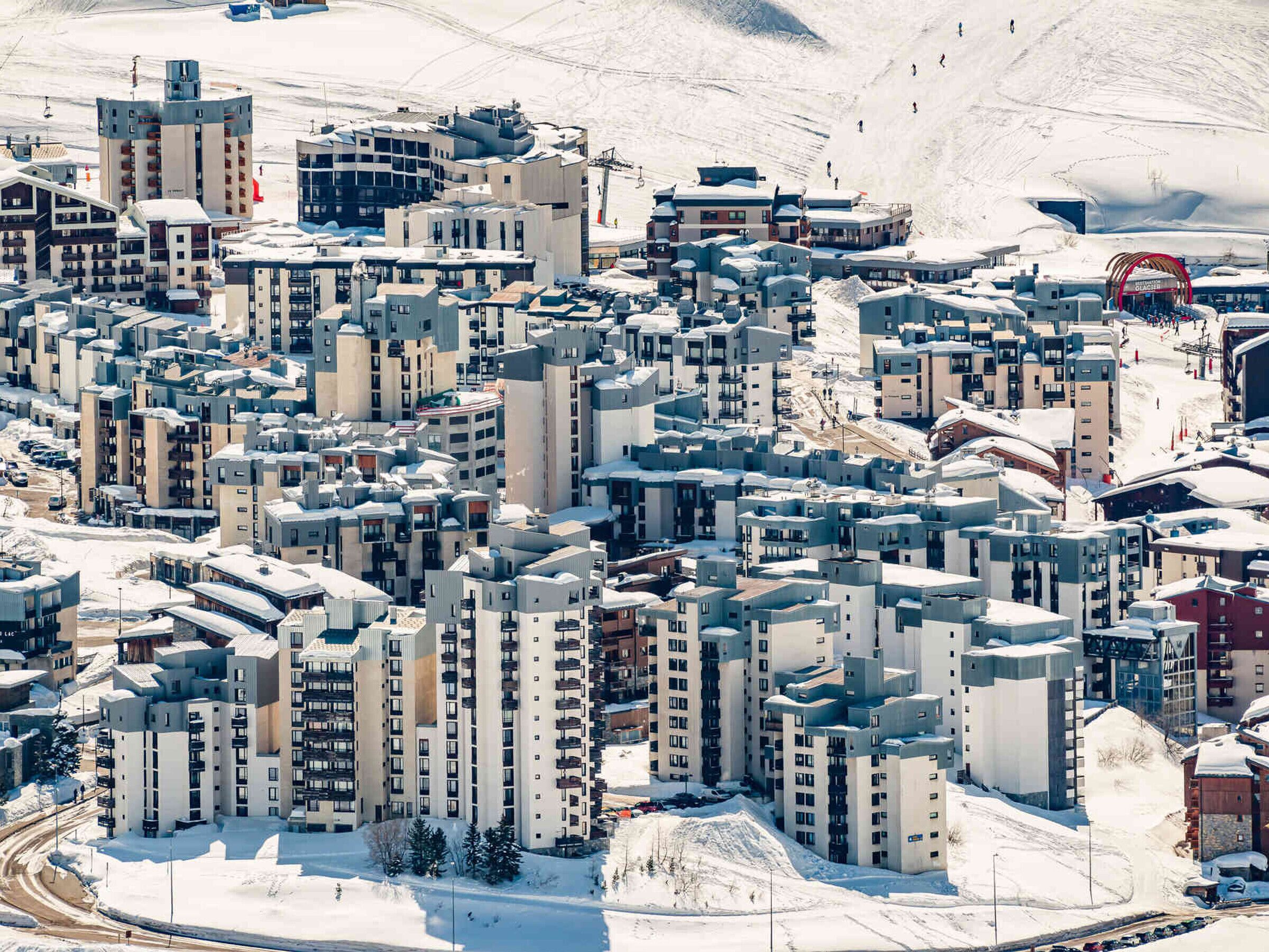 Zona residencial cubierta de nieve con varios edificios altos, un telesilla y una pista de esquí al fondo.