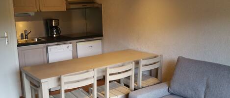 A compact kitchenette with a microwave, coffee maker, and dishwasher. There is a small dining table with chairs and a grey sofa.