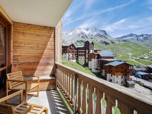A wooden balcony with chairs, overlooking a mountain village with traditional buildings and a clear sky.