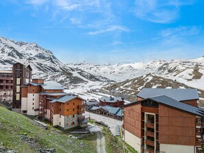 A mountain resort with wooden buildings, a ski lift, and snow-covered peaks in the background.