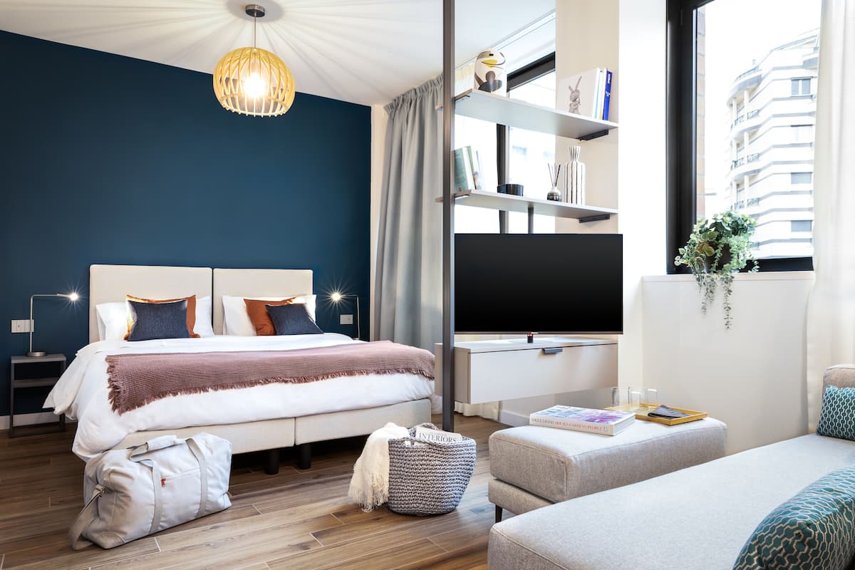 A modern bedroom with a bed, bedside tables, a TV, and a bookshelf.