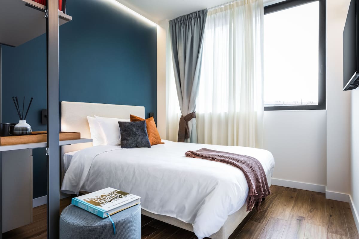 A modern bedroom with a bed, bedside table, and a window with curtains.