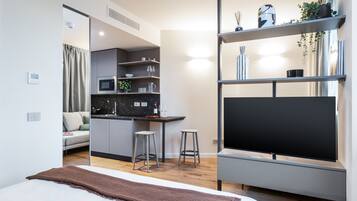 Quarto de hotel moderno com cama, televisão, cozinha compacta e área de estar.