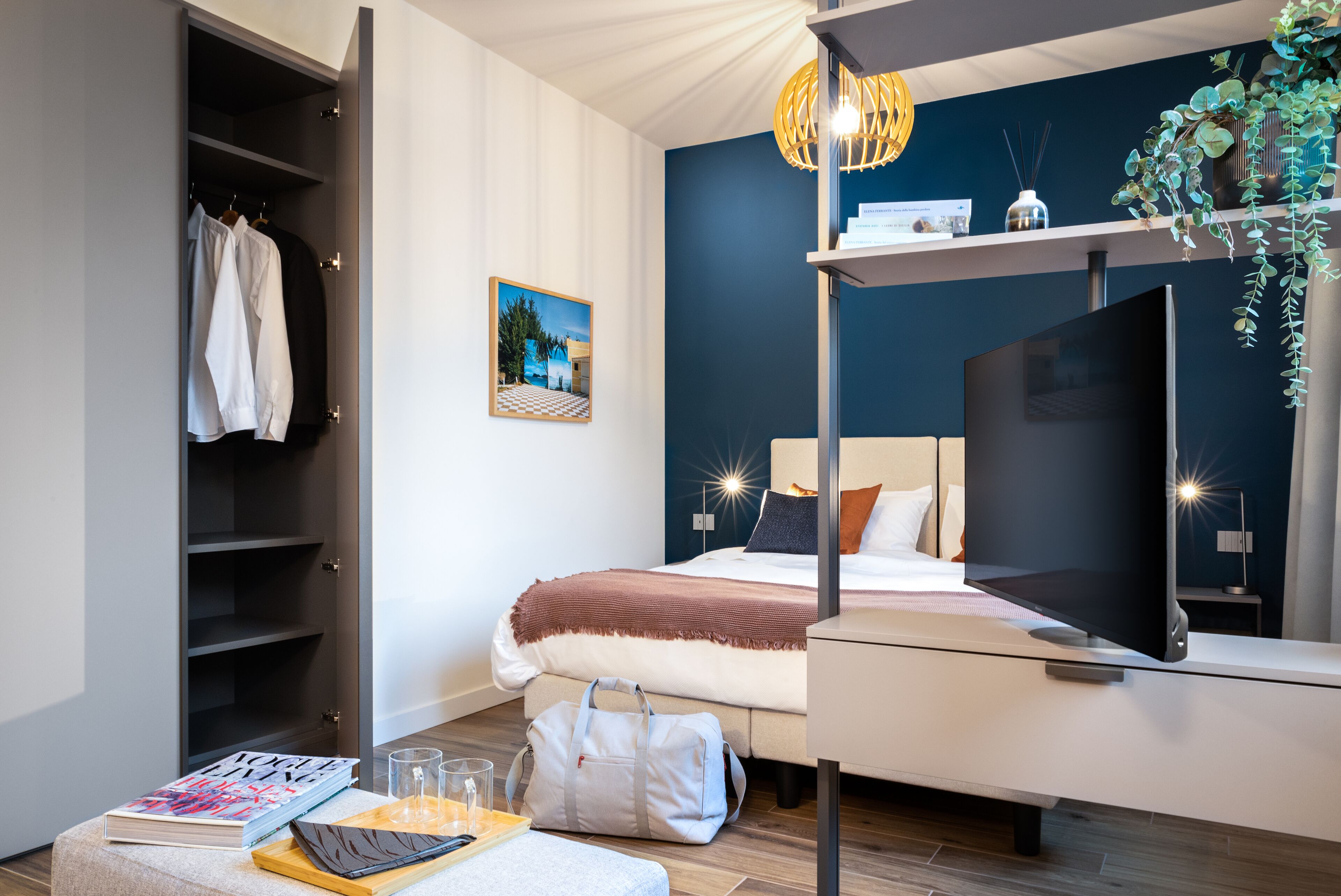 Ein modernes Hotelzimmer mit Bett, Nachttisch, Fernseher und Kleiderschrank.