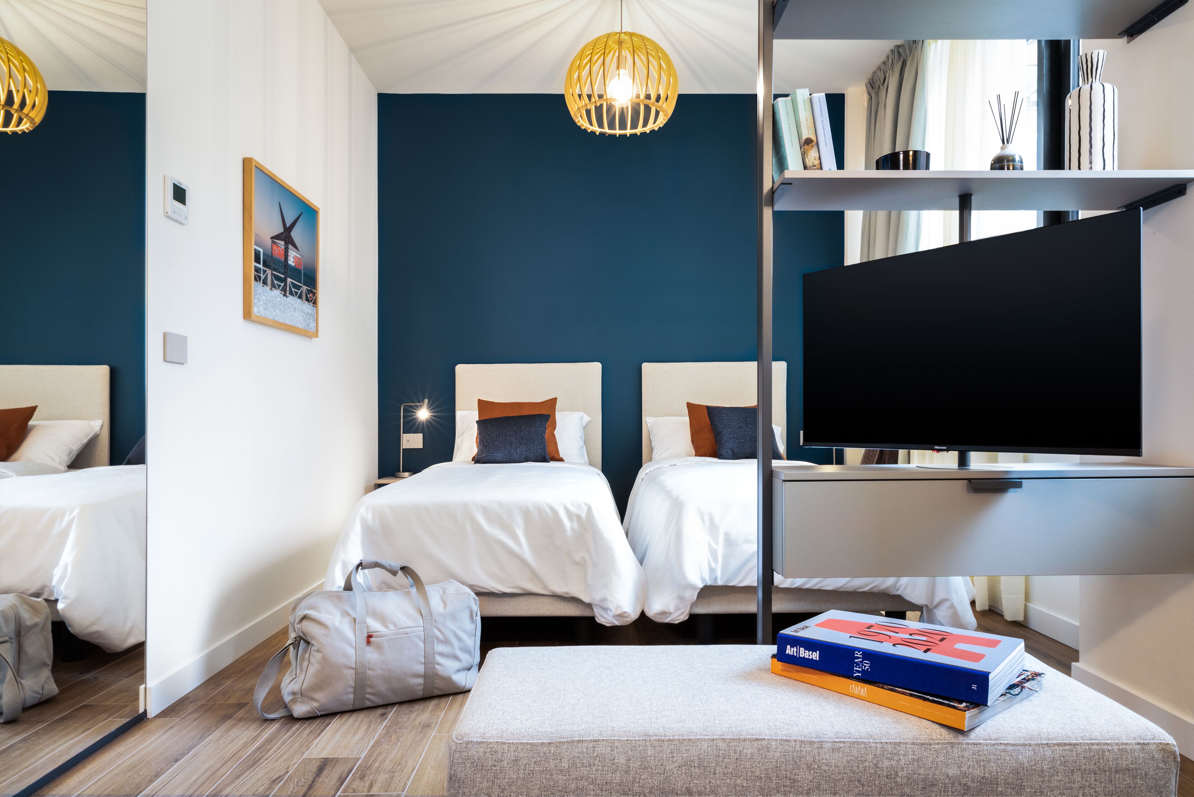 A hotel room with two beds, a TV, a bookshelf, and a painting on the wall.
