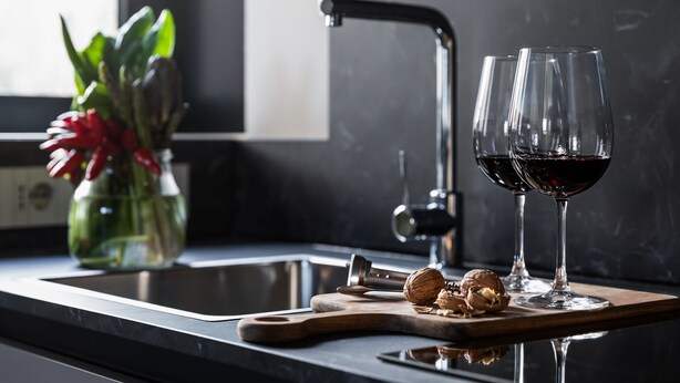 Una encimera de cocina con tabla de cortar, un cascanueces y dos copas de vino tinto.