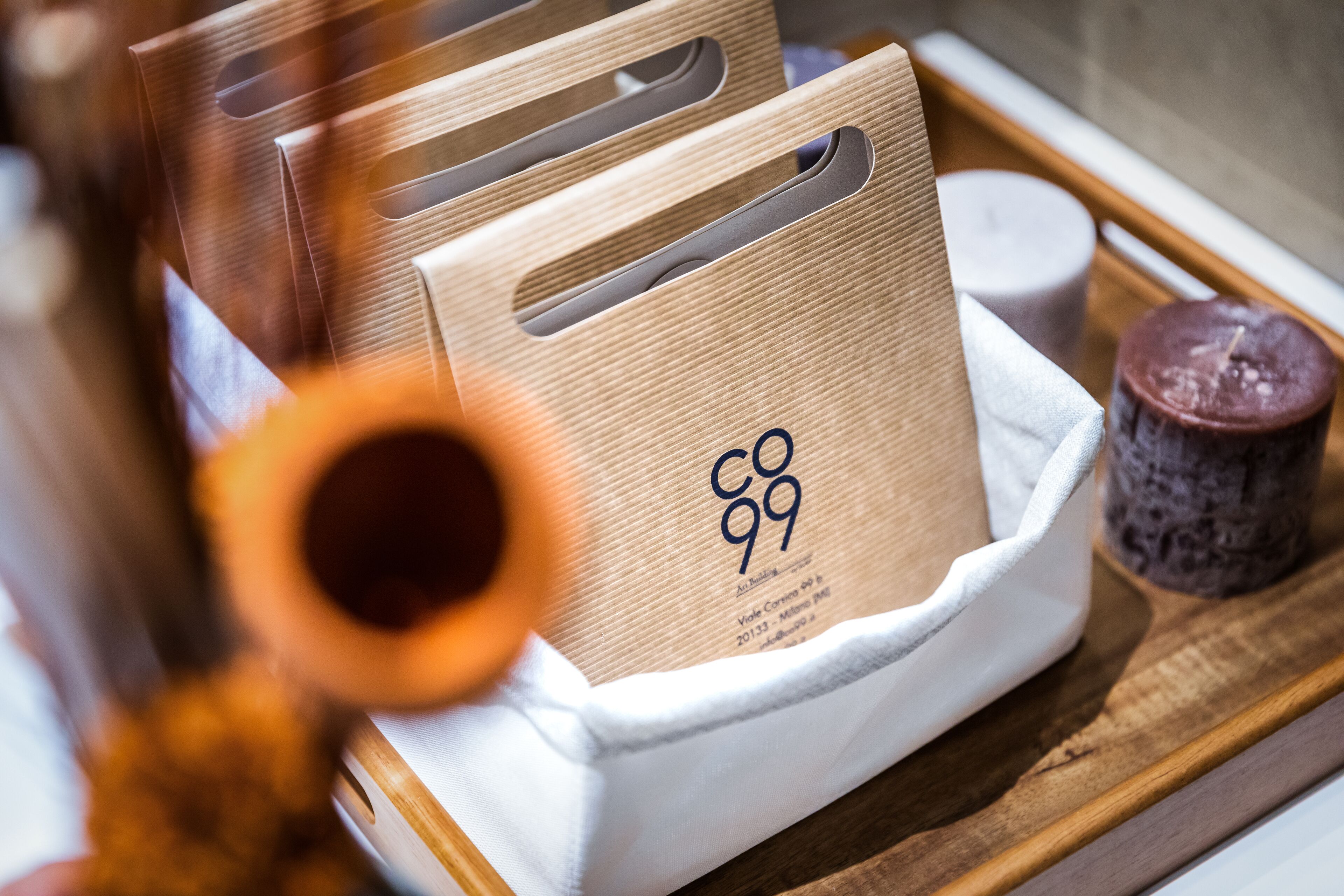 A tray with a white container holding a brown paper bag with a logo, a candle, and a wooden object.