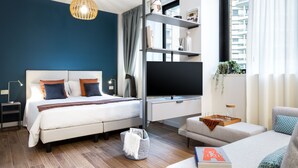 Un dormitorio moderno con cama, televisor y zona de estar, con vistas a la ciudad.